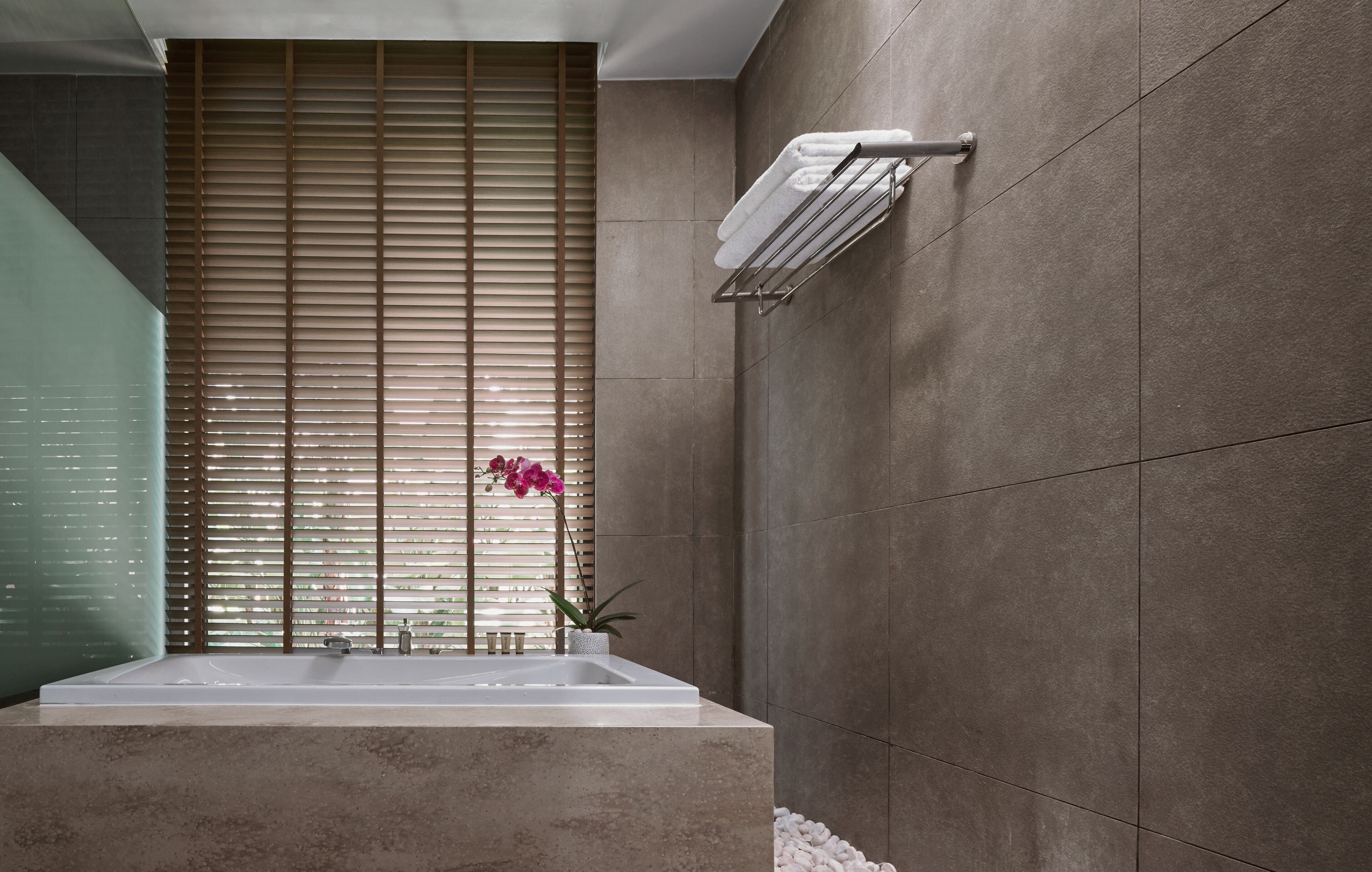 A modern bathroom with a large bathtub, a towel rack, and a potted plant.