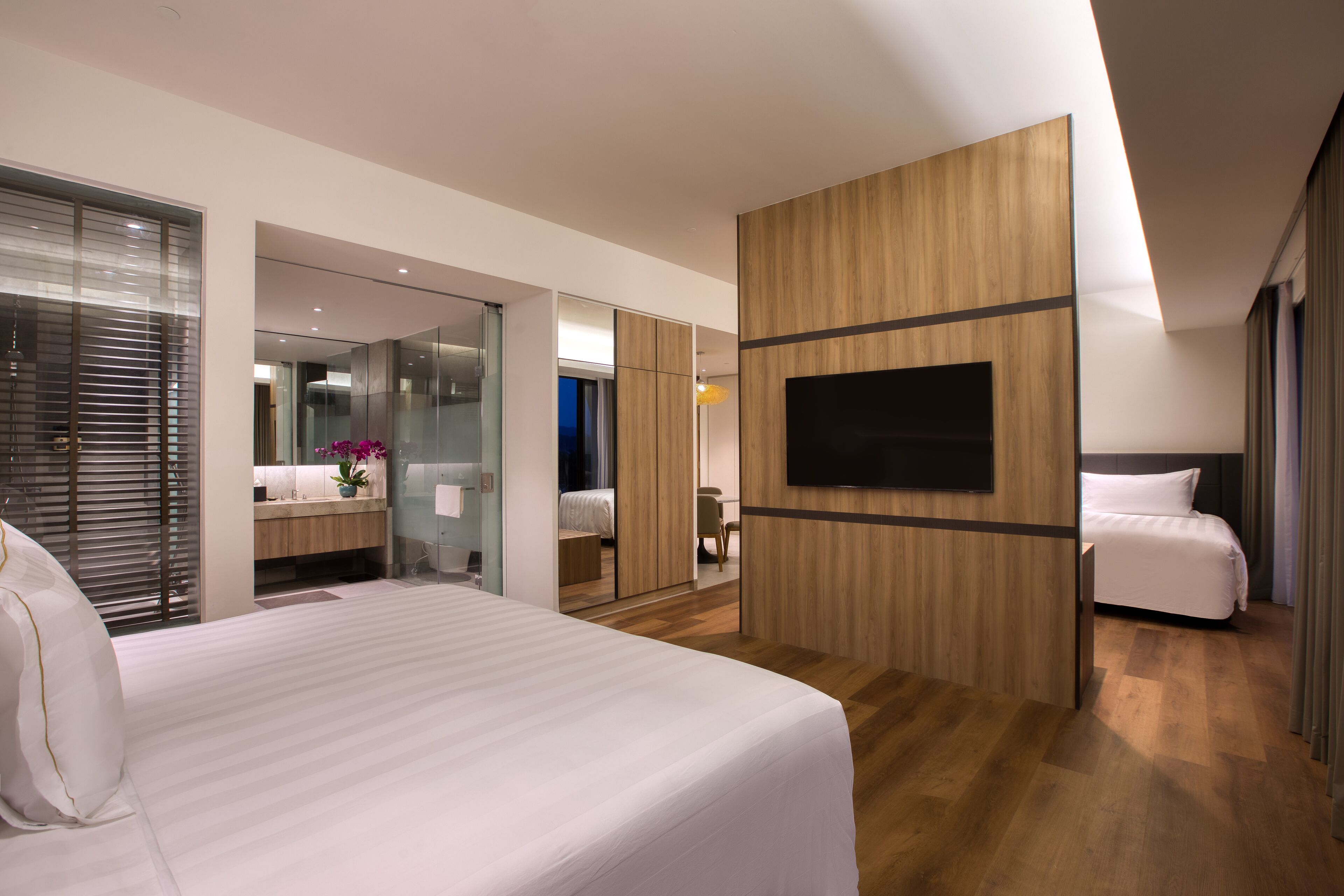 Une chambre d’hôtel moderne dotée d’un grand lit, d’un téléviseur fixé au mur et d’une salle de bain visible à travers une porte en verre.