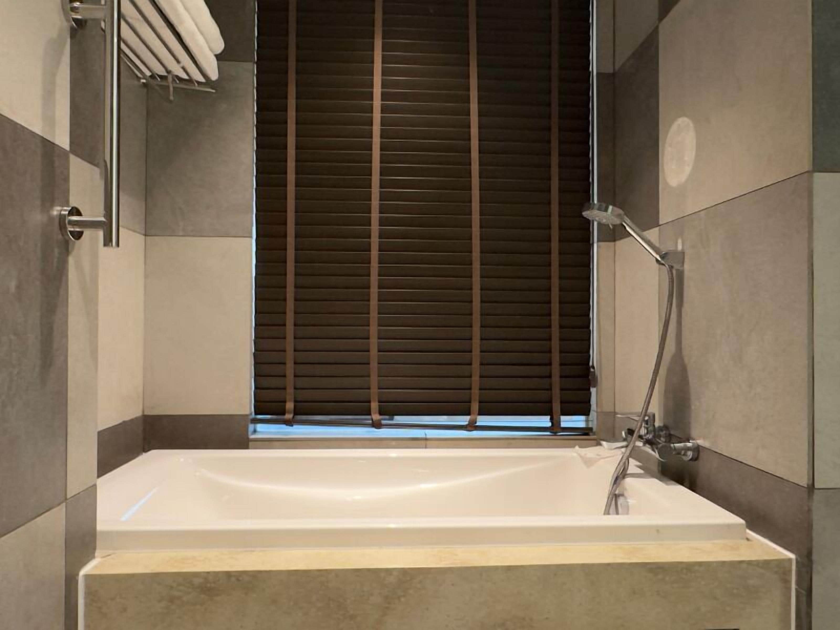 Un baño moderno con bañera, ducha y ventana con persianas.