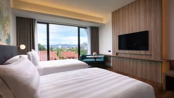 A hotel room with two beds, a TV mounted on the wall, and a view of the cityscape.