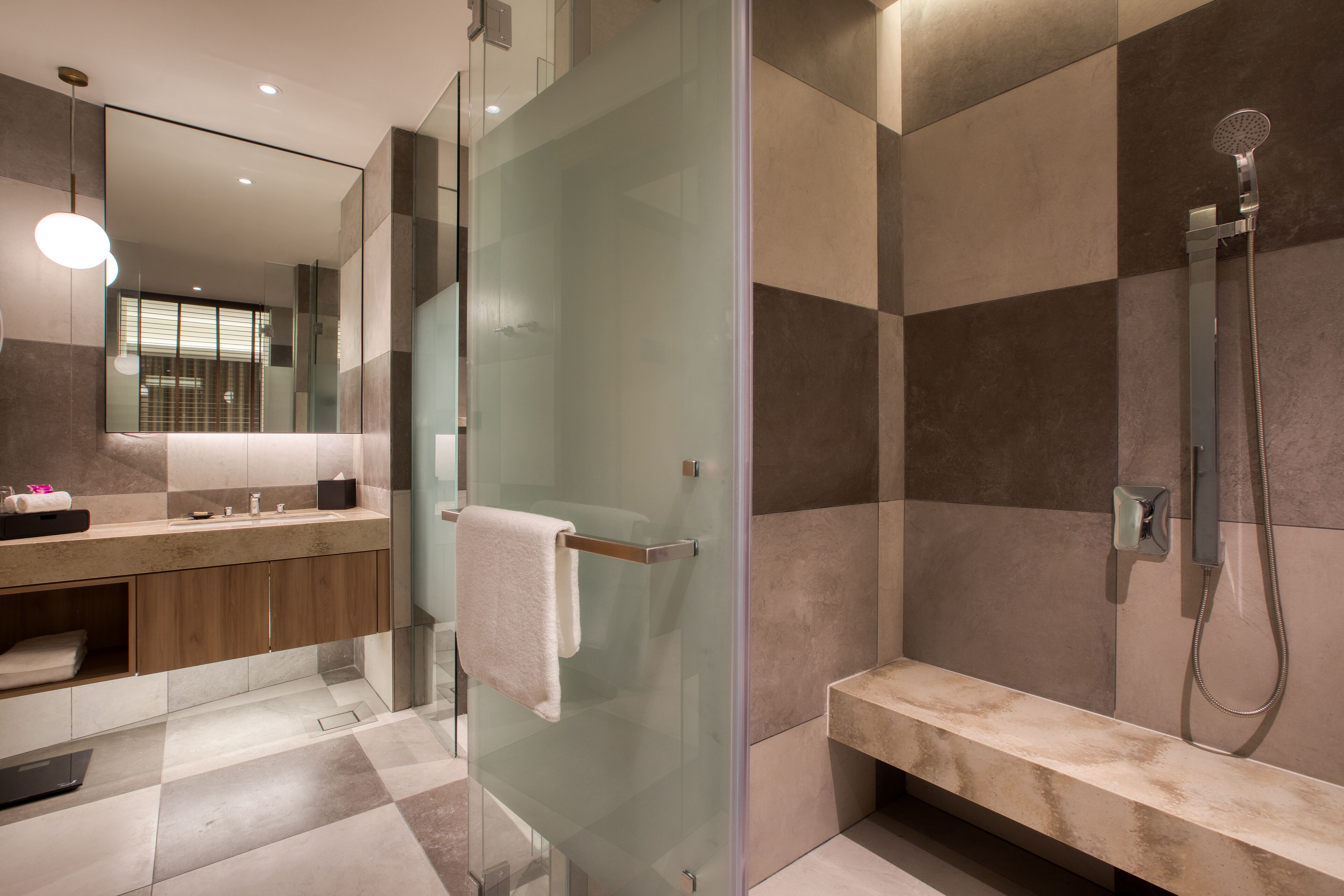 A modern bathroom with a glass shower enclosure, a bench, and a vanity with a mirror.