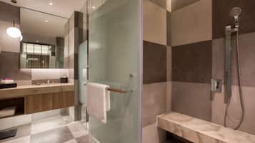 A modern bathroom with a glass shower enclosure, a bench, and a vanity with a mirror.