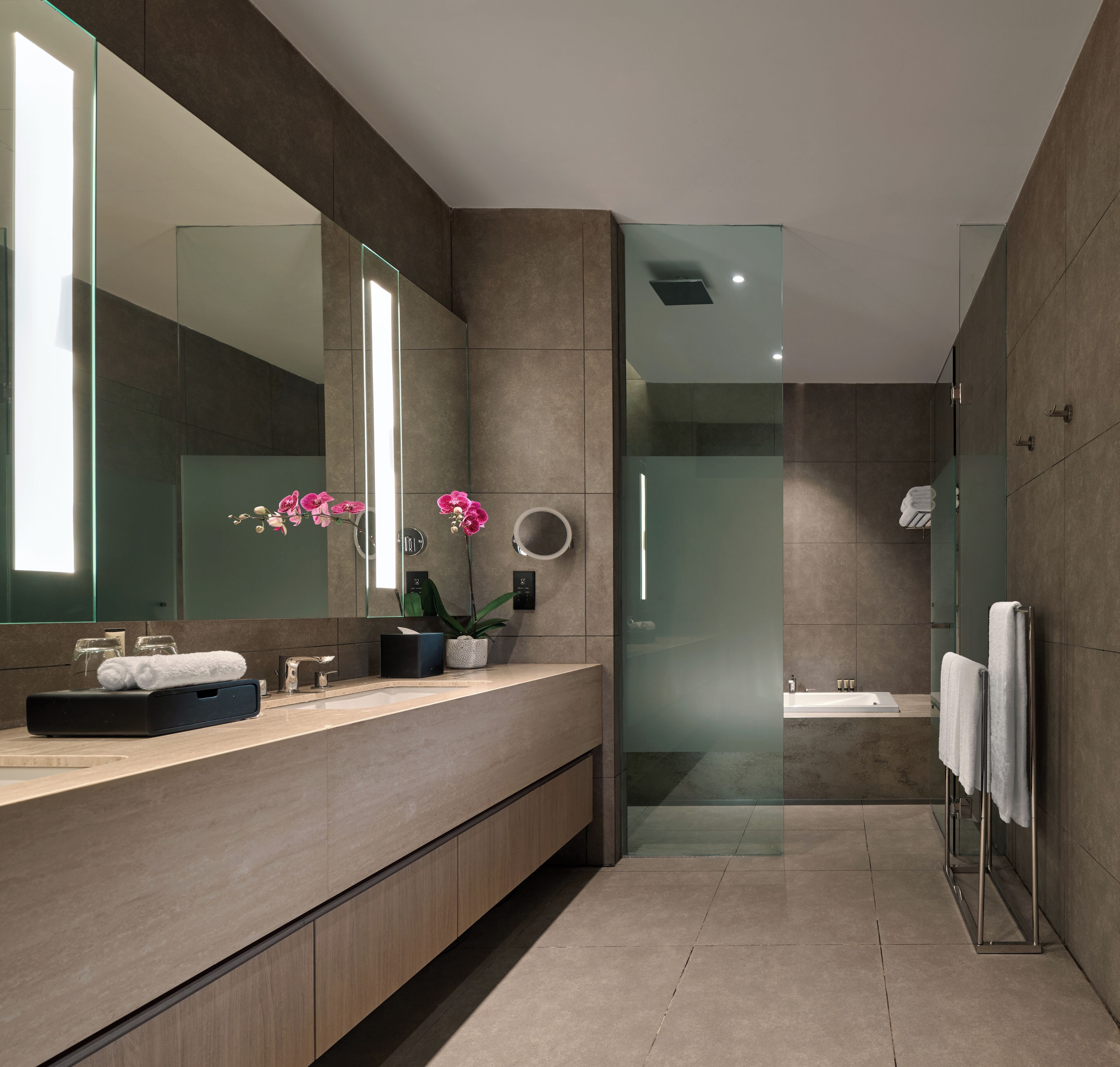 A modern bathroom with a large mirror, a glass shower enclosure, and a vanity with a sink and towel rack.