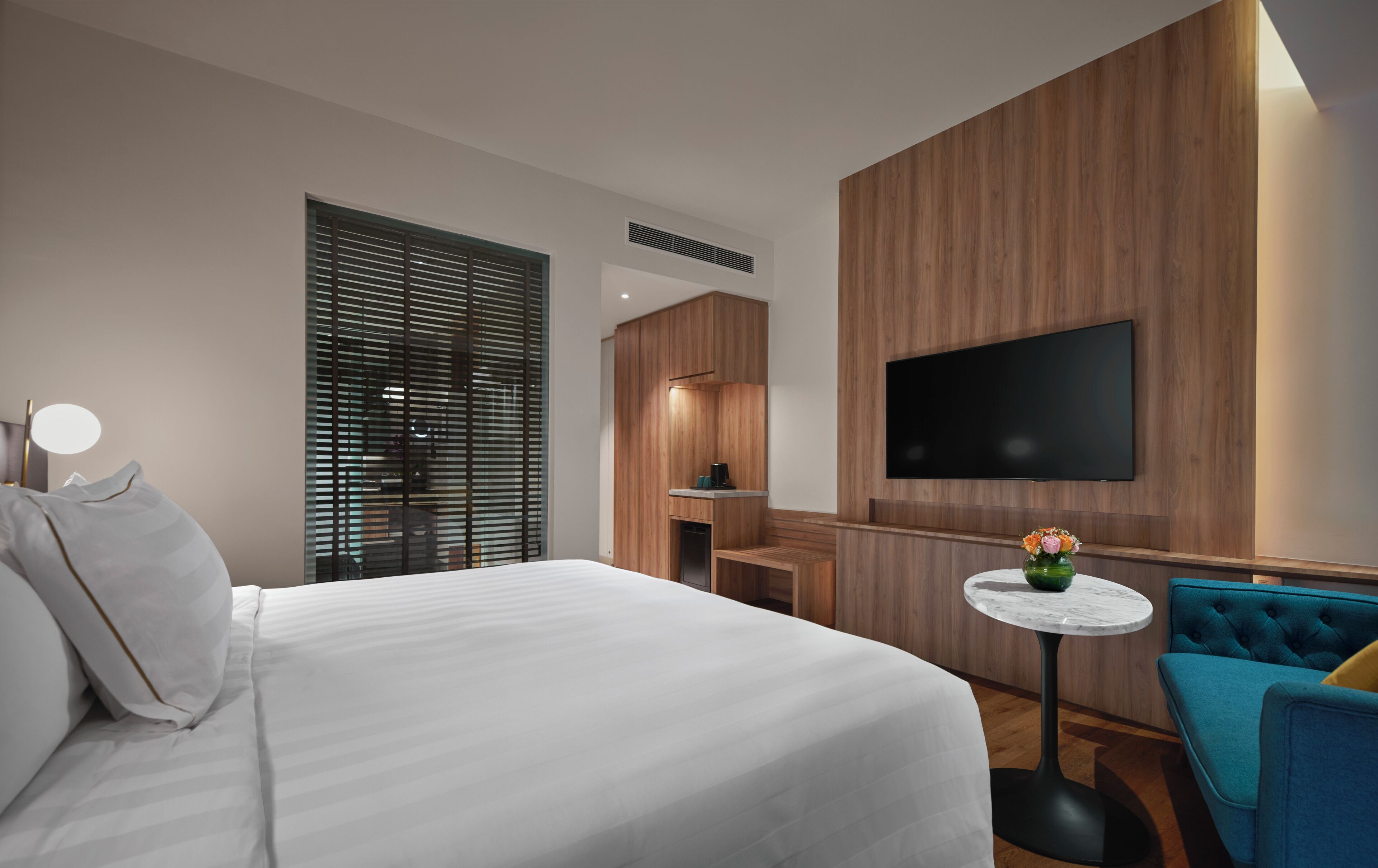 Ein modernes Hotelzimmer mit einem großen Bett, einem kleinen Schreibtisch, einem an der Wand befestigten Fernseher und einem blauen Sessel.