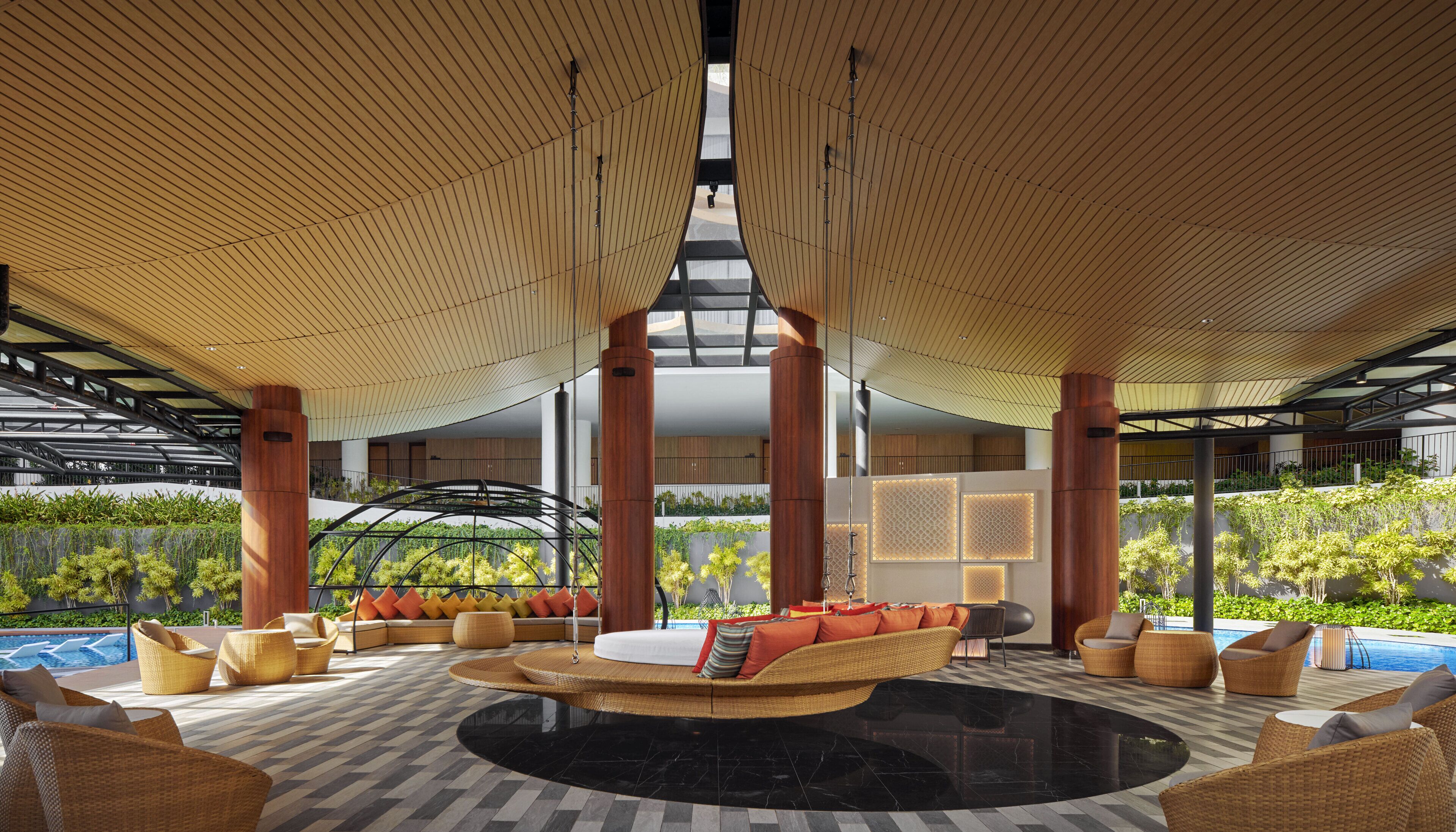 A spacious indoor area with a central seating area, high ceilings, and a view of a pool and greenery.