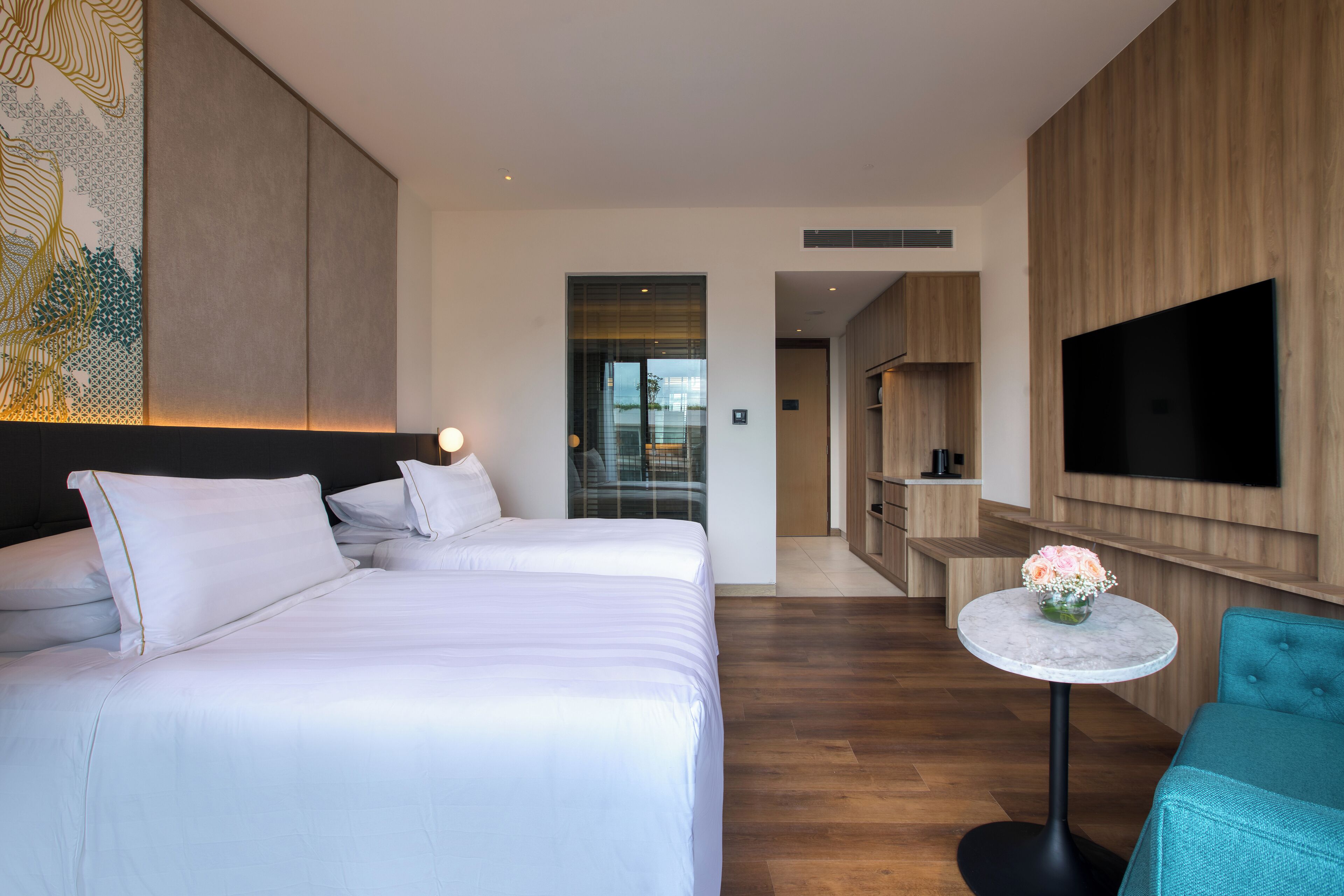 A hotel room with two beds, a TV, a small table with a vase, and a wooden wall panel.