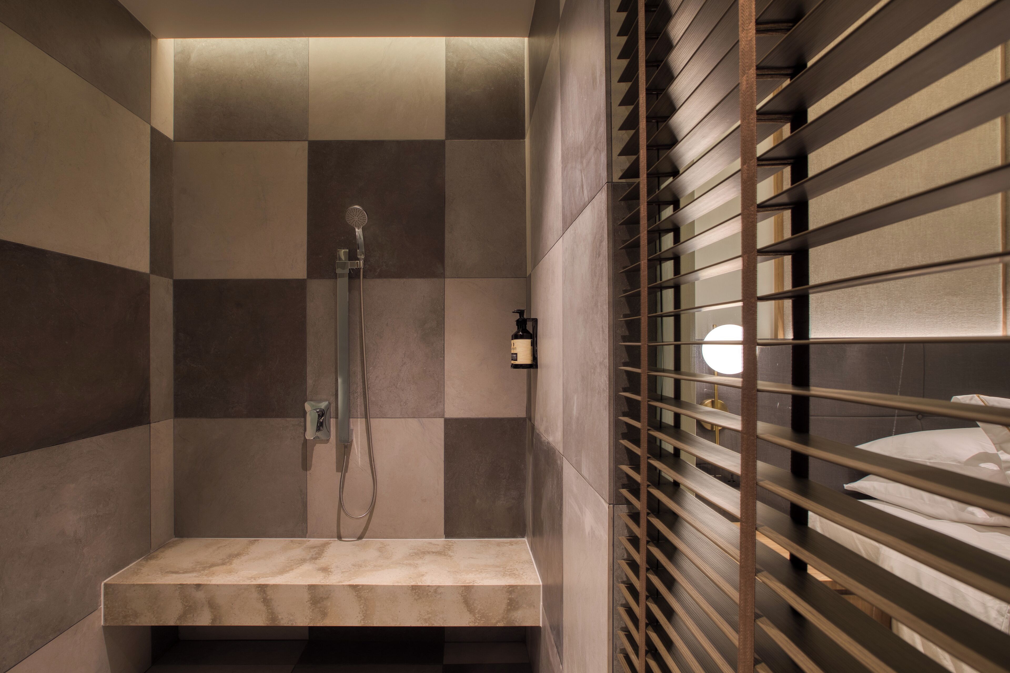 A modern bathroom with a shower, a vanity, and a bed with blinds.