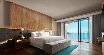 Ett modernt hotellrum med en stor säng, ett träfärgat sänggavel, ett skrivbord och utsikt över havet.