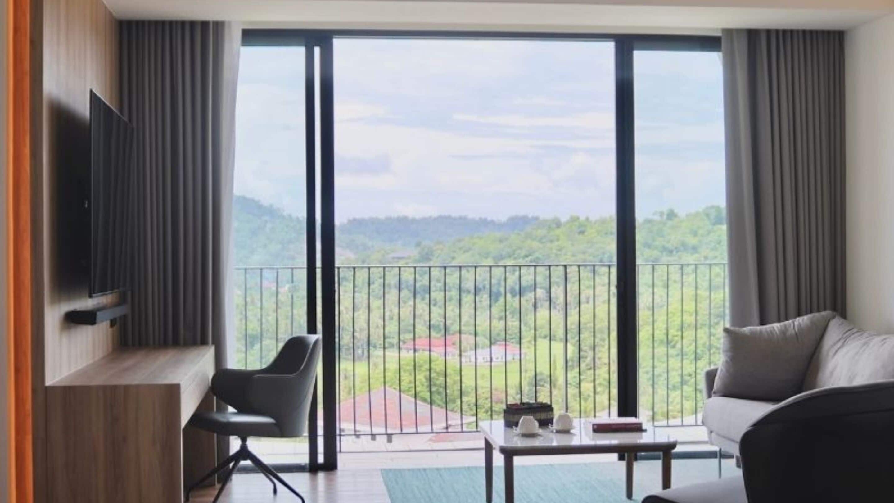 A modern hotel room with a large sliding glass door leading to a balcony with a view of a green landscape.