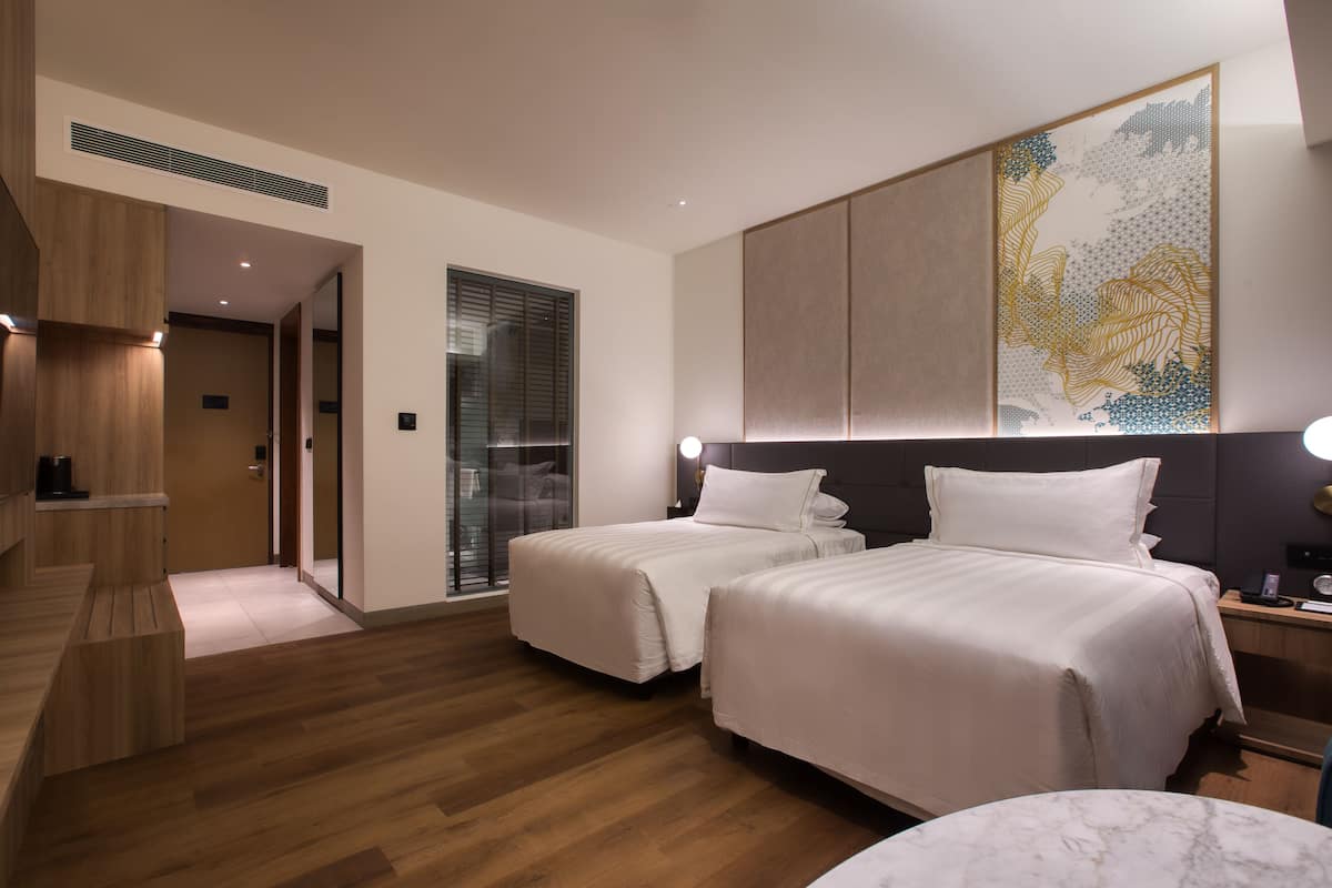 Une chambre d’hôtel avec deux lits, un banc en bois, une table en marbre et un grand tableau abstrait accroché au mur.