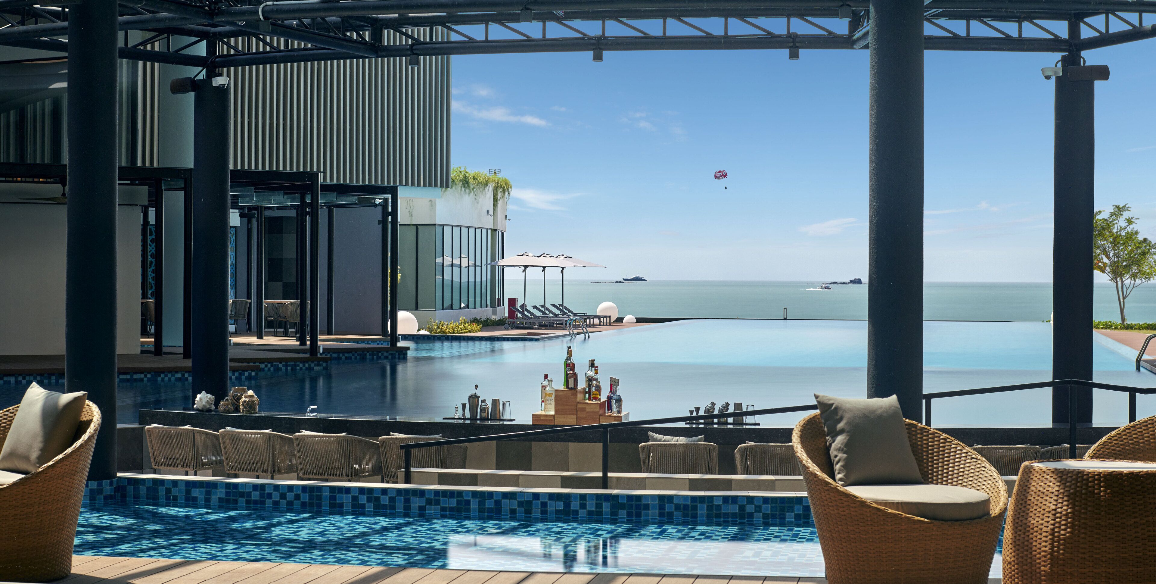A poolside area with lounge chairs, a bar, and a view of the sea.