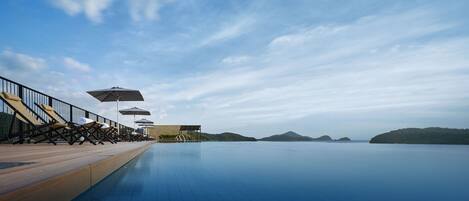 A serene infinity pool with lounge chairs and umbrellas, overlooking a calm sea and distant islands.
