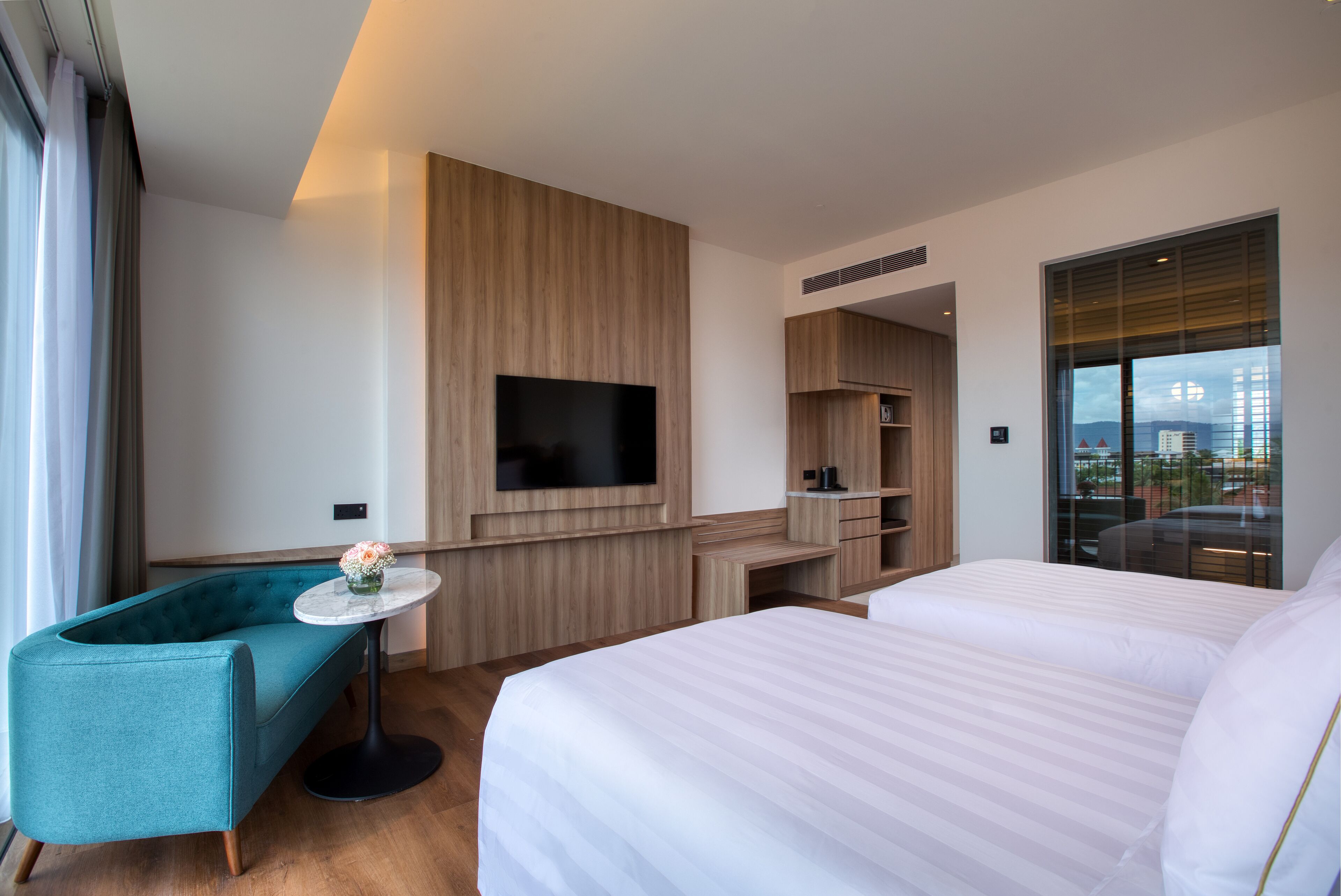 A modern hotel room with a large bed, a sofa, a TV mounted on the wall, and a city view through the window.