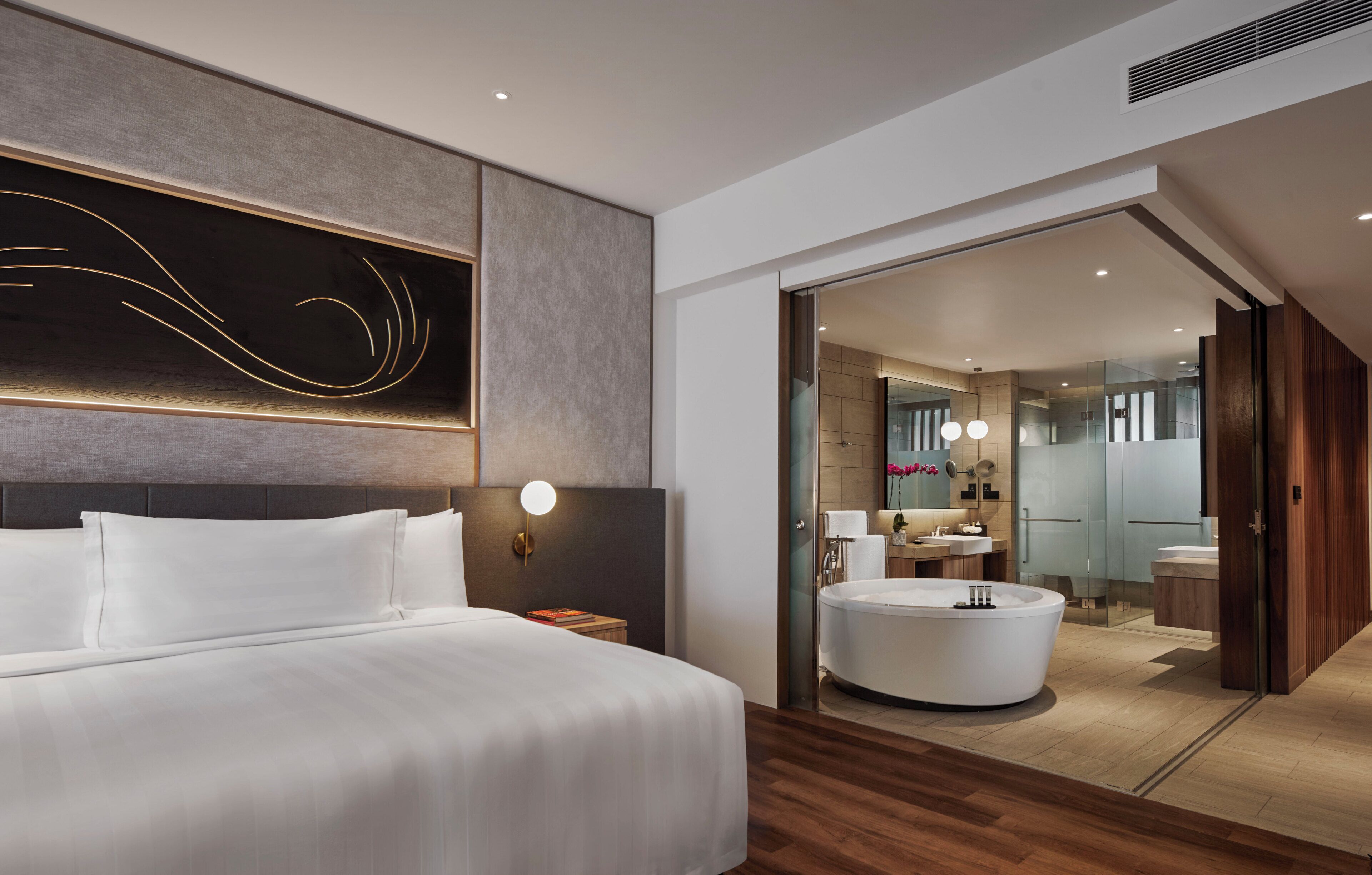 A modern hotel room with a large bed, a round bathtub, and a glass-enclosed bathroom.