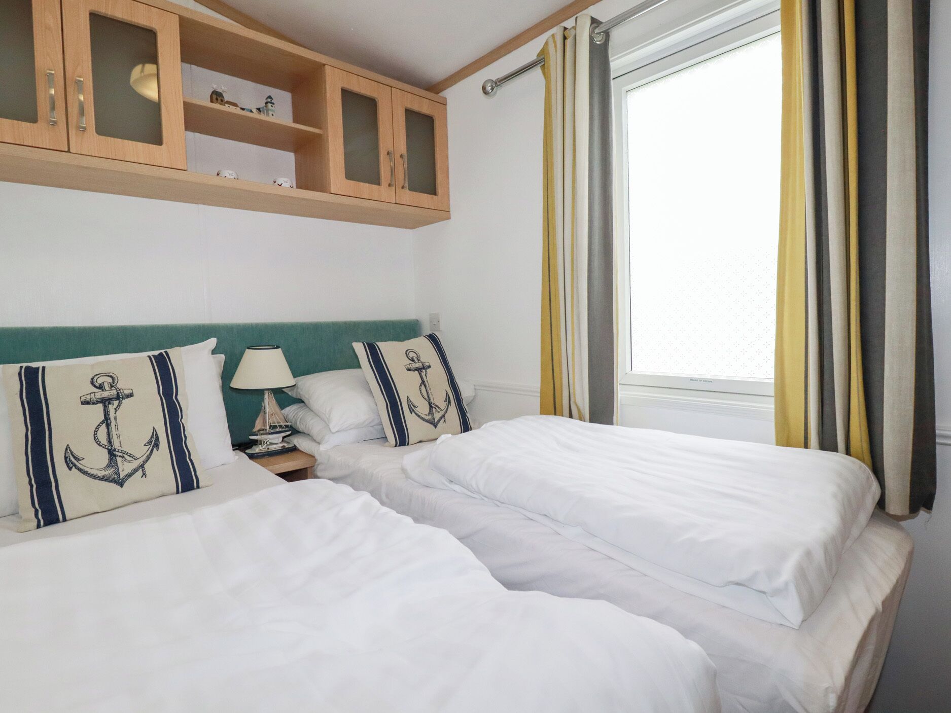 A hotel room with two beds, a nightstand, a lamp, and a window with curtains.