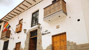 A building with a white facade, multiple wooden doors, and a balcony with a railing. - Hotel Montecristo Cusco (Cusco)