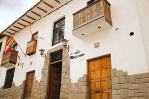A building with a white facade, multiple wooden doors, and a balcony with a railing.