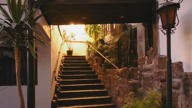 A stone staircase leading to a brightly lit entrance, surrounded by potted plants and a stone wall. - Hotel Montecristo Cusco (Cusco)