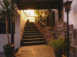 A stone staircase leading to a brightly lit entrance, surrounded by potted plants and a stone wall.