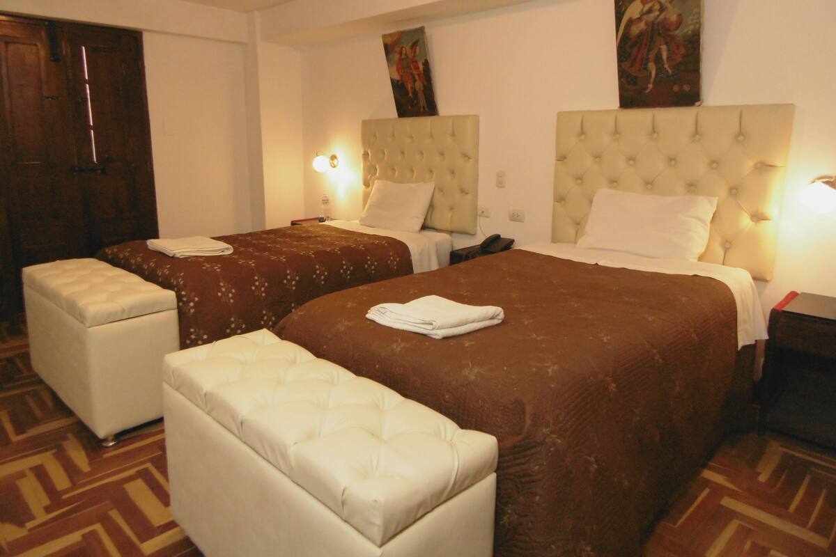 A hotel room with two beds, a small seating area, and artwork on the walls.