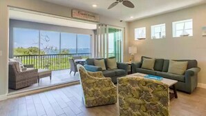 A spacious living room with a large sliding glass door leading to a balcony, a ceiling fan, and a sign reading "Coastal Cove."