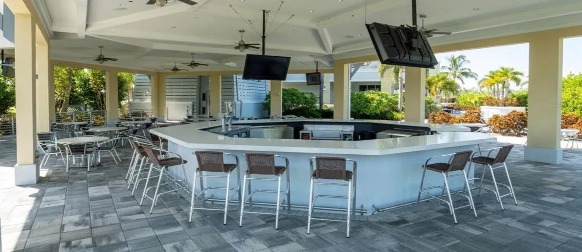 An outdoor bar area with a central island, bar stools, ceiling fans, and a flat-screen TV.