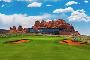 A modern building with a glass facade, surrounded by a well-manicured golf course and red rock formations.