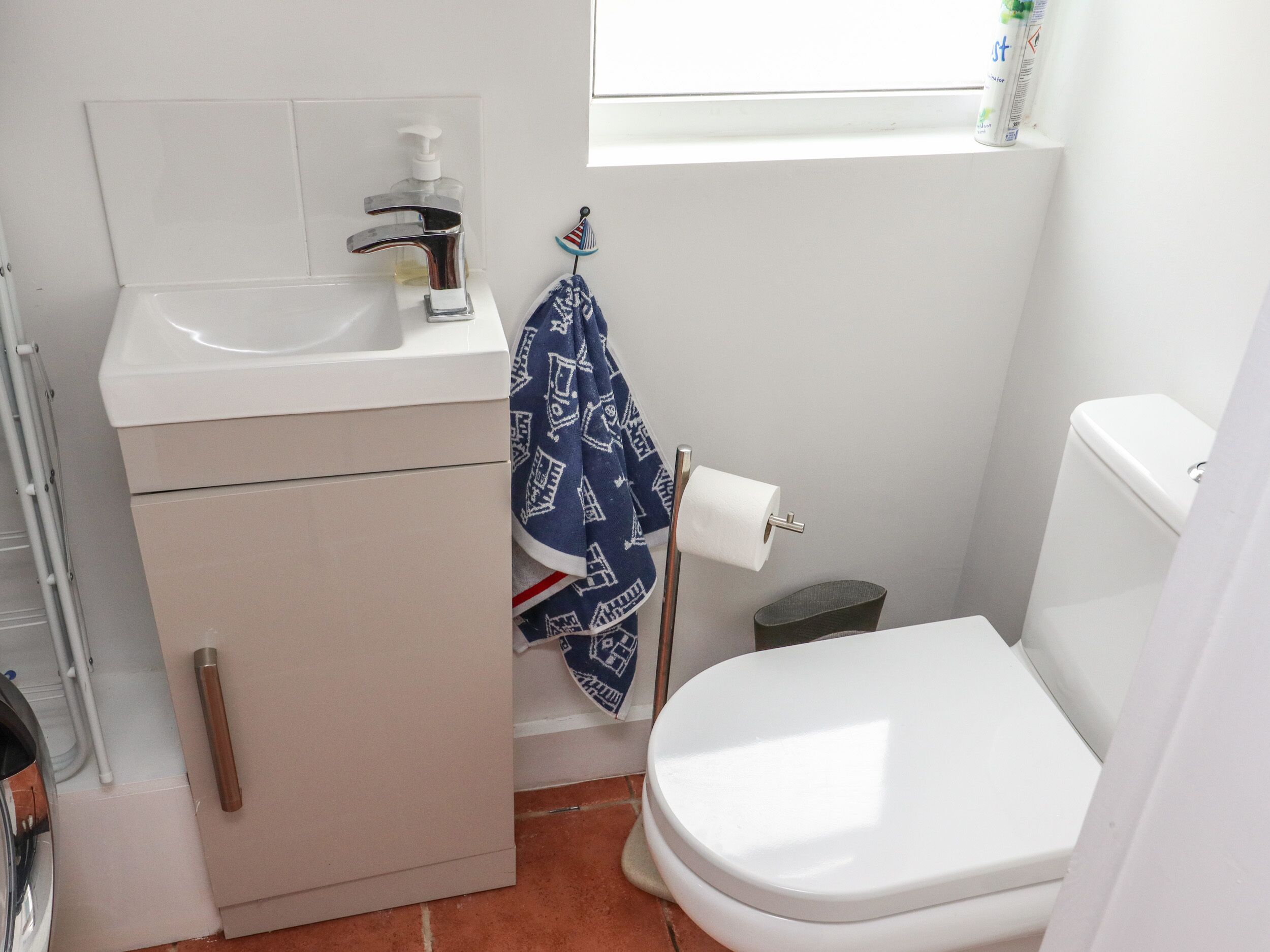 A small bathroom with a white sink, toilet, and a window above the toilet.
