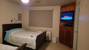 A bedroom with a bed, a ceiling fan, a TV, a window with blinds, a radiator, and a door. - Private Beachfront House (Cabo Rojo)