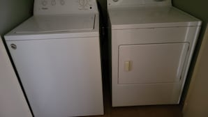 Two white front-loading washing machines in a laundry room with a green wall and a visible electrical outlet. - Private Beachfront House (Cabo Rojo)