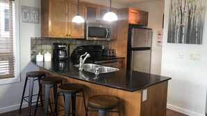 Une cuisine moderne avec des meubles en bois, un plan de travail noir, des appareils en acier inoxydable et un coin bar avec des tabourets.