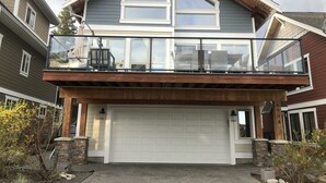 Une maison à deux étages avec un grand garage, un balcon doté de rampes en verre et des fondations en pierre.