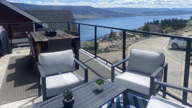 Un balcon donnant sur un lac, une table, deux chaises et une plante en pot.