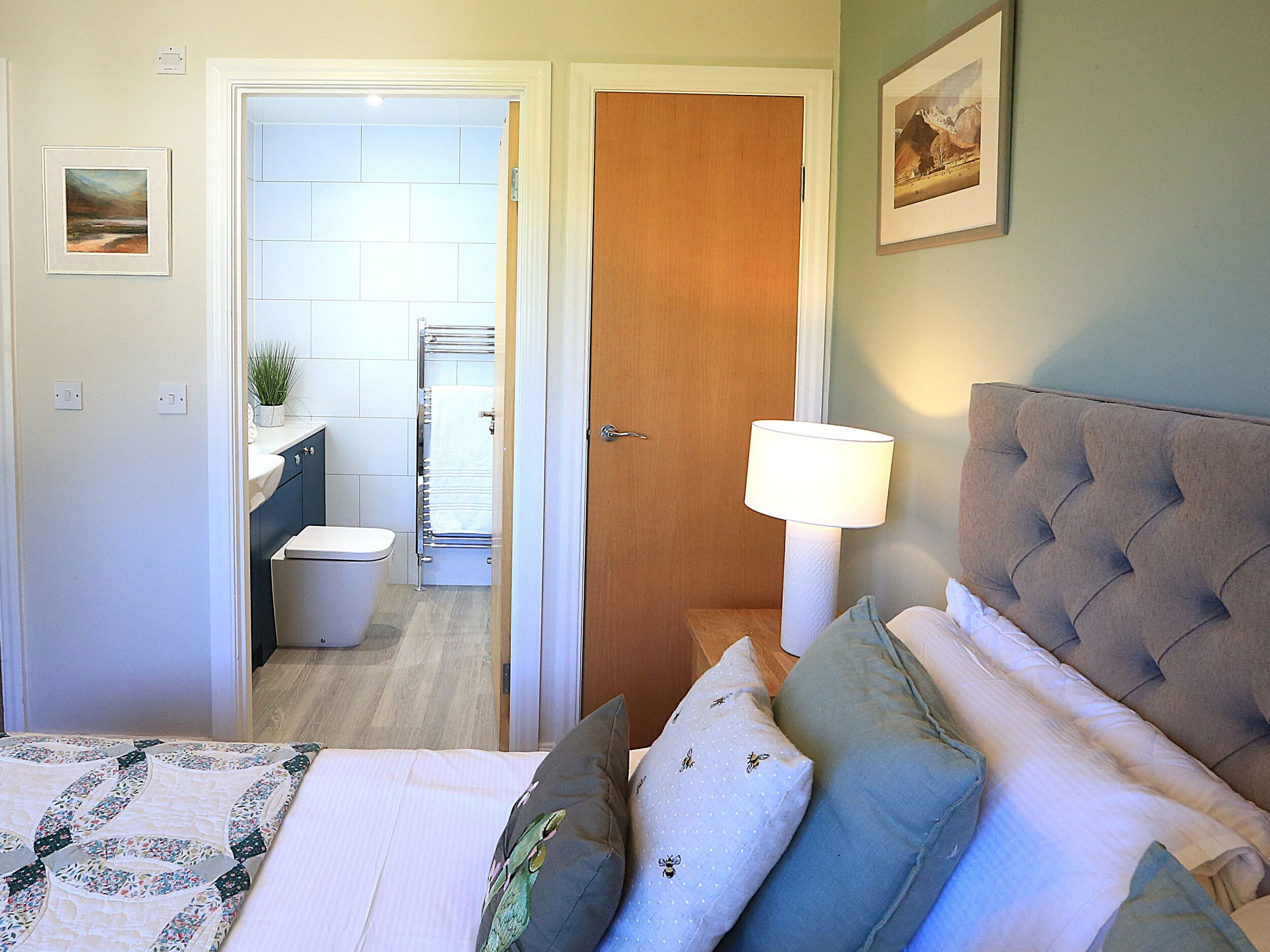 A bedroom with a bed, pillows, a bedside lamp, and a view into the bathroom.