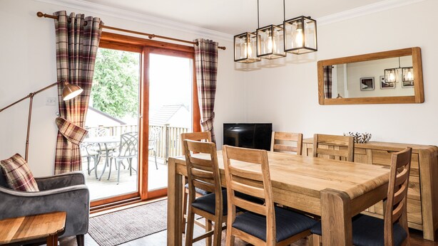 Een eetruimte met een houten tafel en stoelen, een televisie en een spiegel aan de muur.