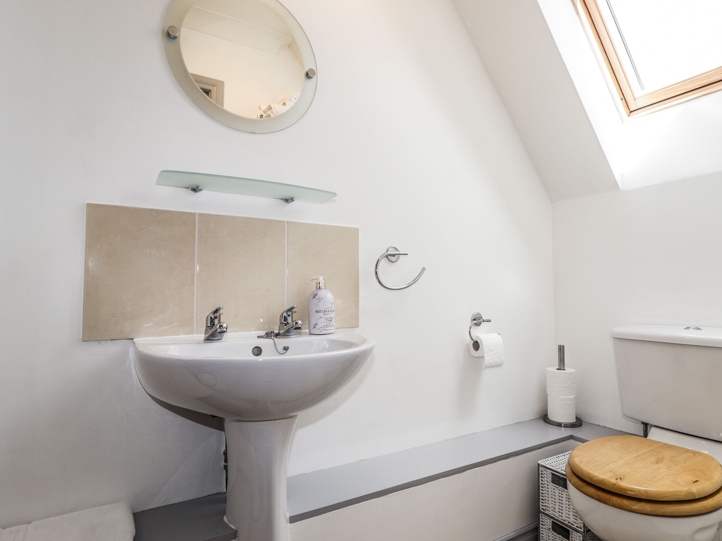 A modern bathroom with a pedestal sink, a toilet, and a mirror.
