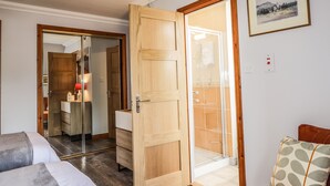 Een hotelkamer met een houten deur, een douchecabine van glas, een bed, een nachtkastje en een ingelijst schilderij aan de muur.