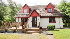 Een huis met twee verdiepingen, een rood dak, een houten terras en een voordeur.