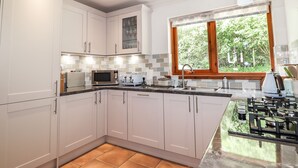 Een moderne keuken met witte kasten, een roestvrijstalen magnetron, een gasfornuis en een raam met uitzicht op groen.