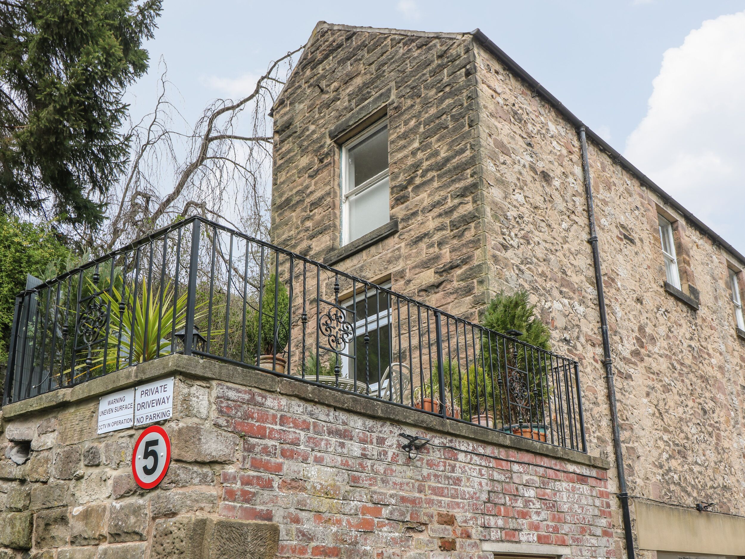 A stone building with a metal balcony railing, a warning sign, and a no parking sign.