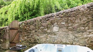 A hot tub with a control panel, a wooden door, and a stone wall in a garden setting. - Kirkham House (Matlock)