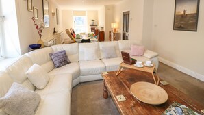 A spacious living room with a white sectional sofa, a wooden coffee table, and a dining area in the background. - Kirkham House (Matlock)