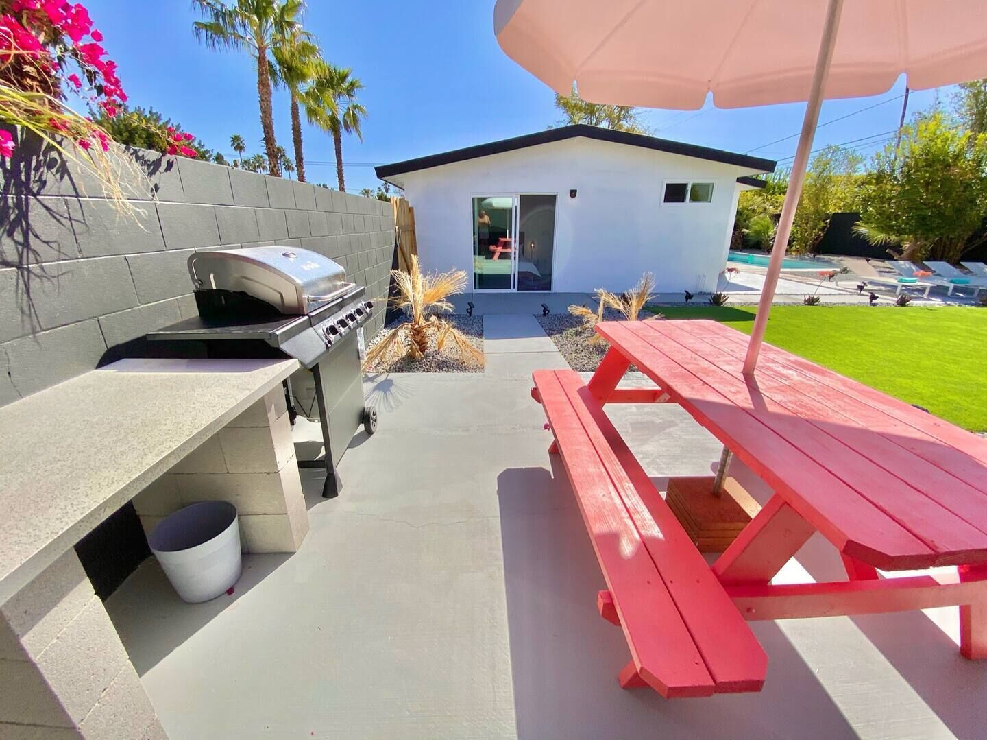 An outdoor barbecue area with a grill, a picnic table, and a small house in the background.