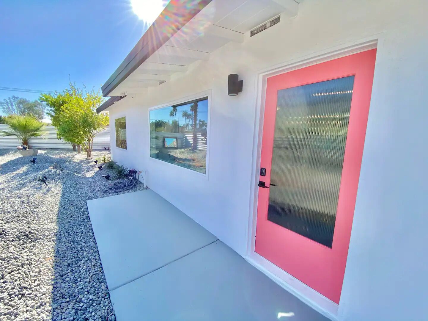 A modern building with a red door, a small window, and a concrete pathway.