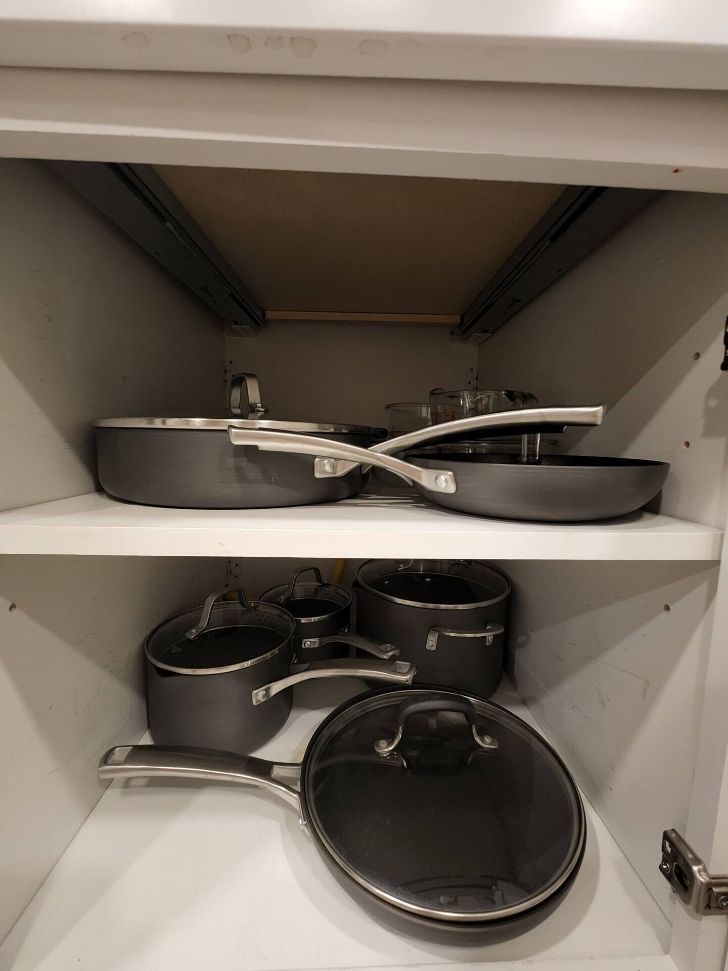 A kitchen with white cabinets, a stove, and various pots and pans stored on shelves.
