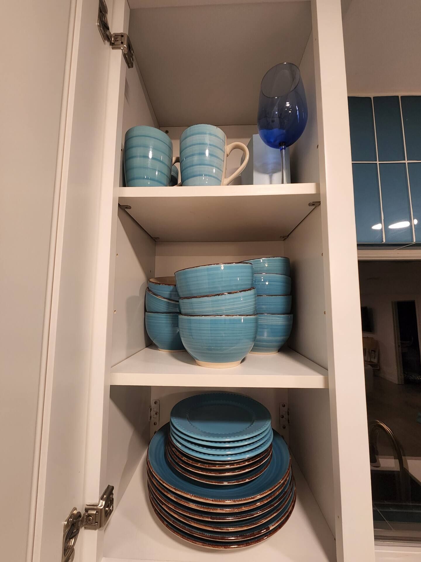 A kitchen cabinet with shelves holding blue ceramic dishes and a glass vase.