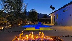 A pool with a blue and yellow color scheme, surrounded by a fire feature, and a building with a white exterior.