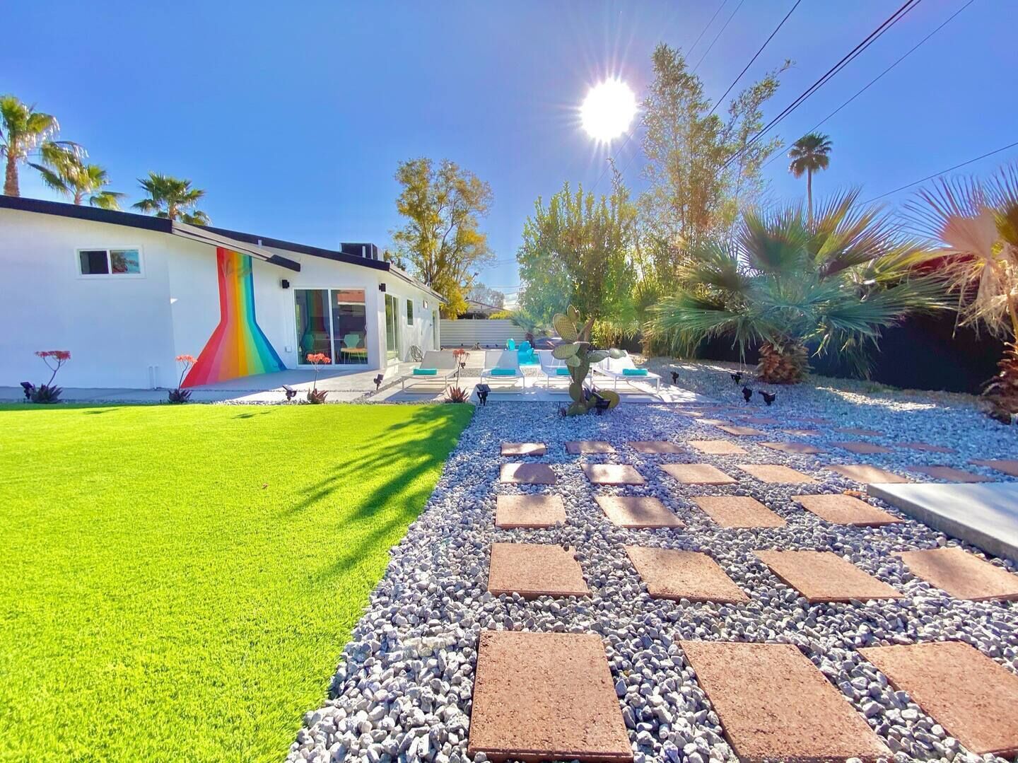 Une maison moderne ornée d’une fresque colorée, dotée d’une pelouse bien entretenue et d’un espace patio aménagé avec des sièges.