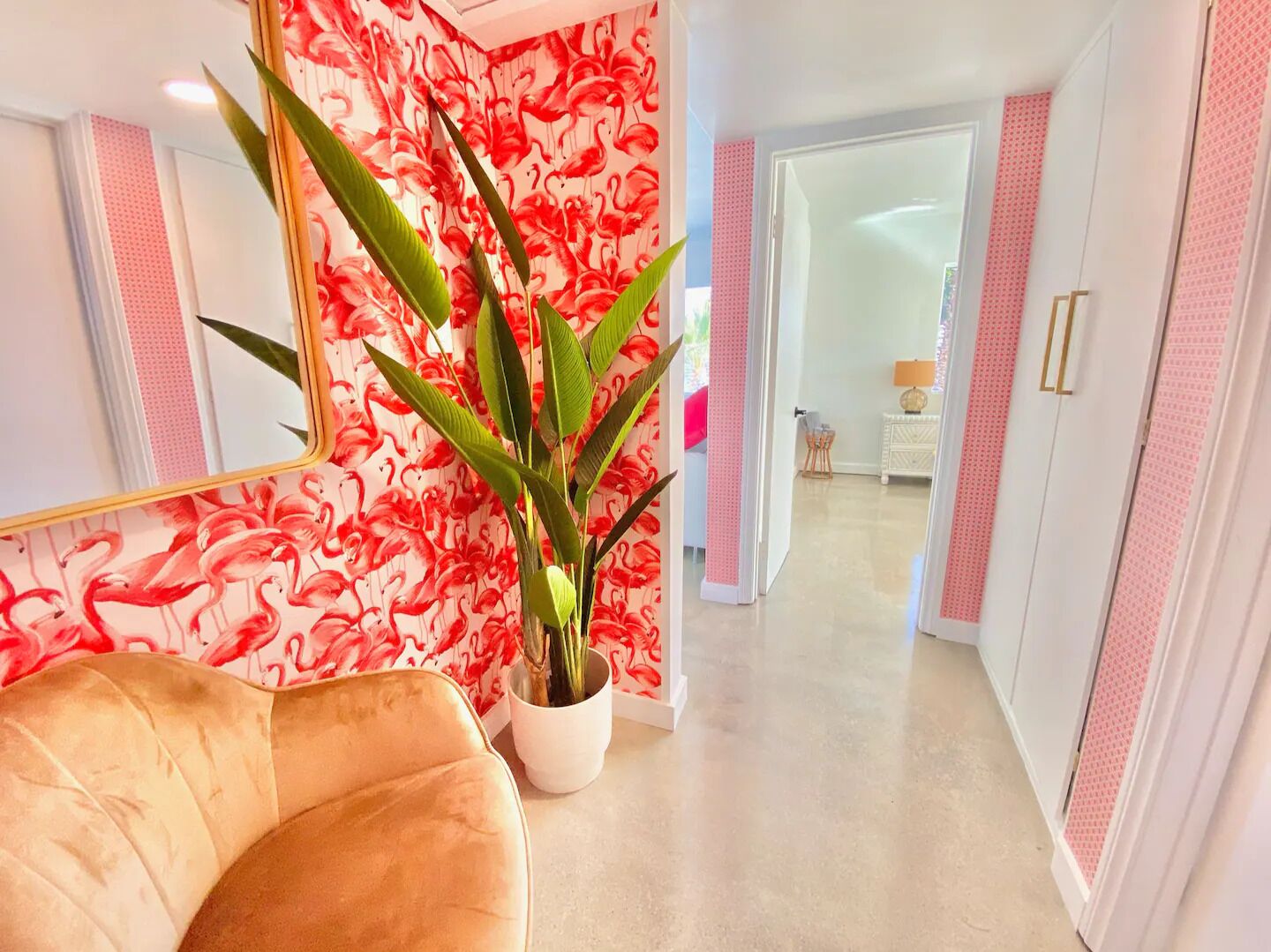 A hallway with a mirrored wall, a large potted plant, and a beige sofa.