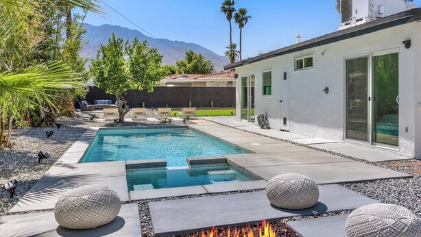 A modern pool area with a fire pit, outdoor seating, and a view of mountains.